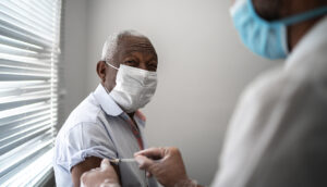 Nurse applying vaccine on patient's arm using face mask